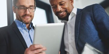 Shot of two businessmen using a digital tablet together at work  Our Services financial projections Copy 360x180